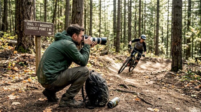 Photographer capturing mountain biker on forest trail